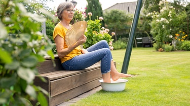 Senioren kühlt im Garten ihre Füße in einem Wasserbad.  | Bild: picture alliance