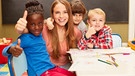 Fröhliche Schulkinder umringen eine Frau und recken alle den Daumen in die Höhe. | Bild: picture alliance / Zoonar | Robert Kneschke